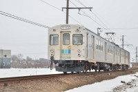 まだ雪が残る津軽路を水間鉄道ラッピングの列車が駆け抜けます。